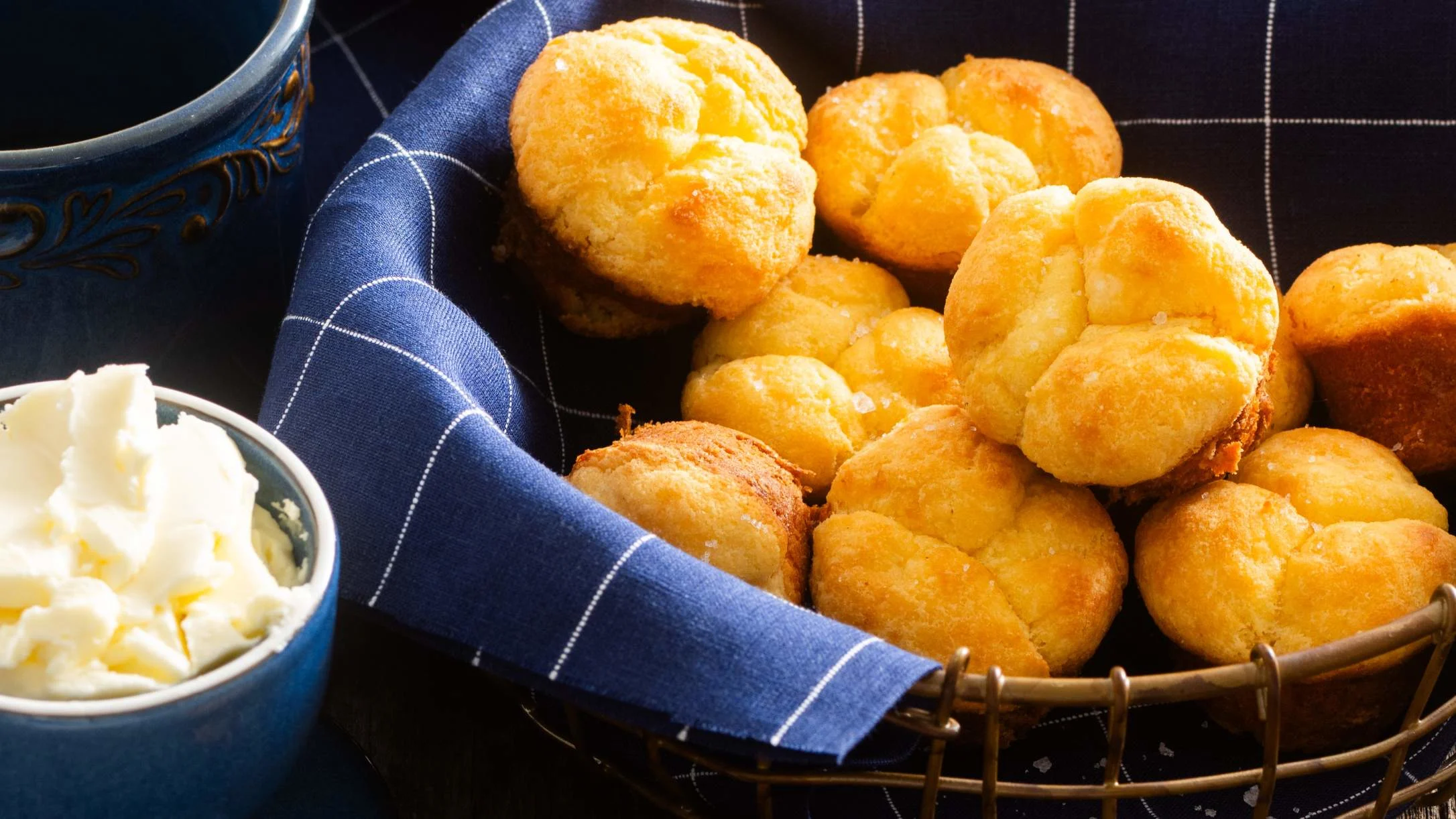 Golden keto rolls in a basket with blue checkered napkin, served with butter in a small blue dish.