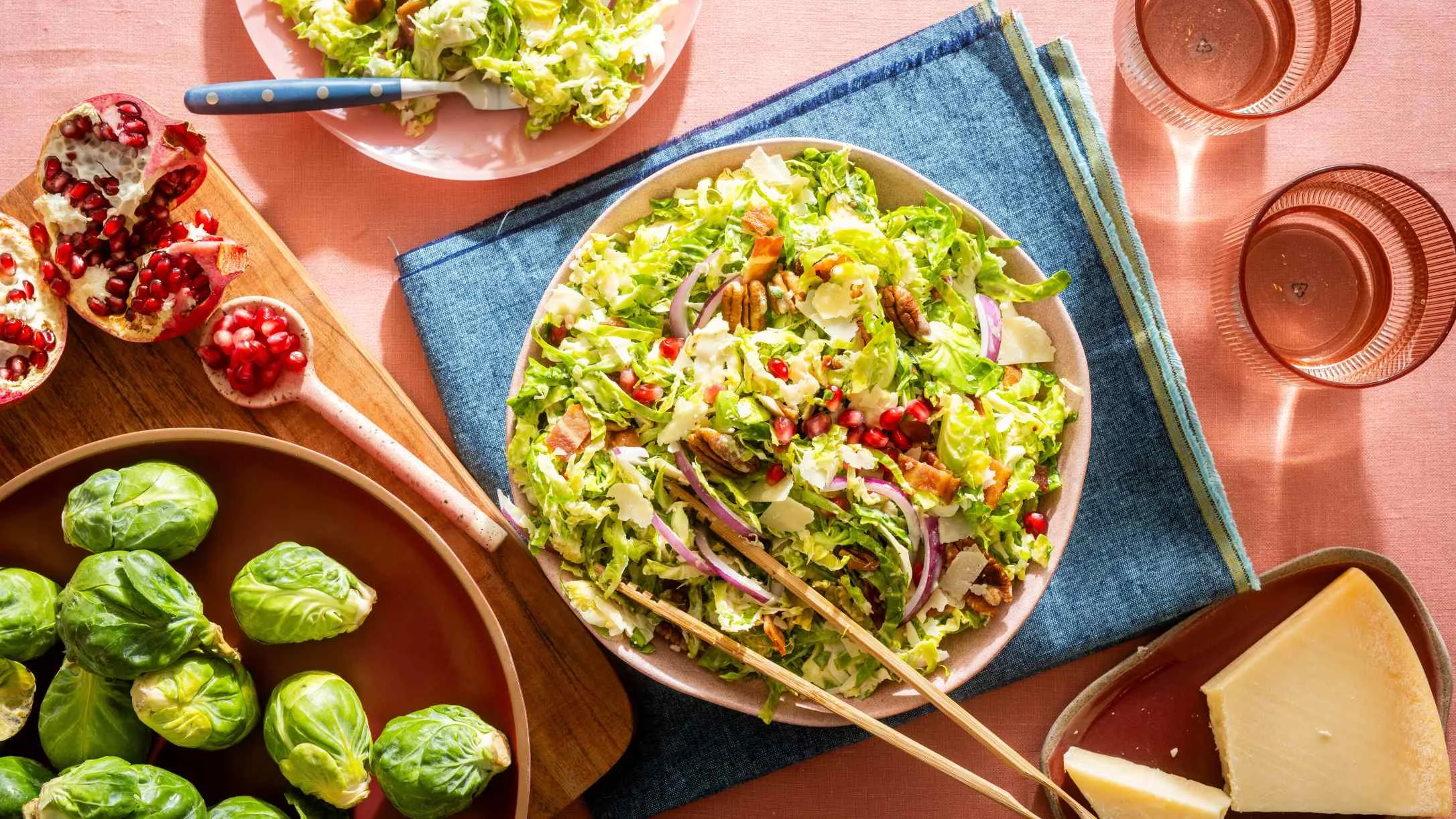 Fresh green salad with pomegranate seeds and nuts, surrounded by brussels sprouts, cheese, and rose-colored glasses.