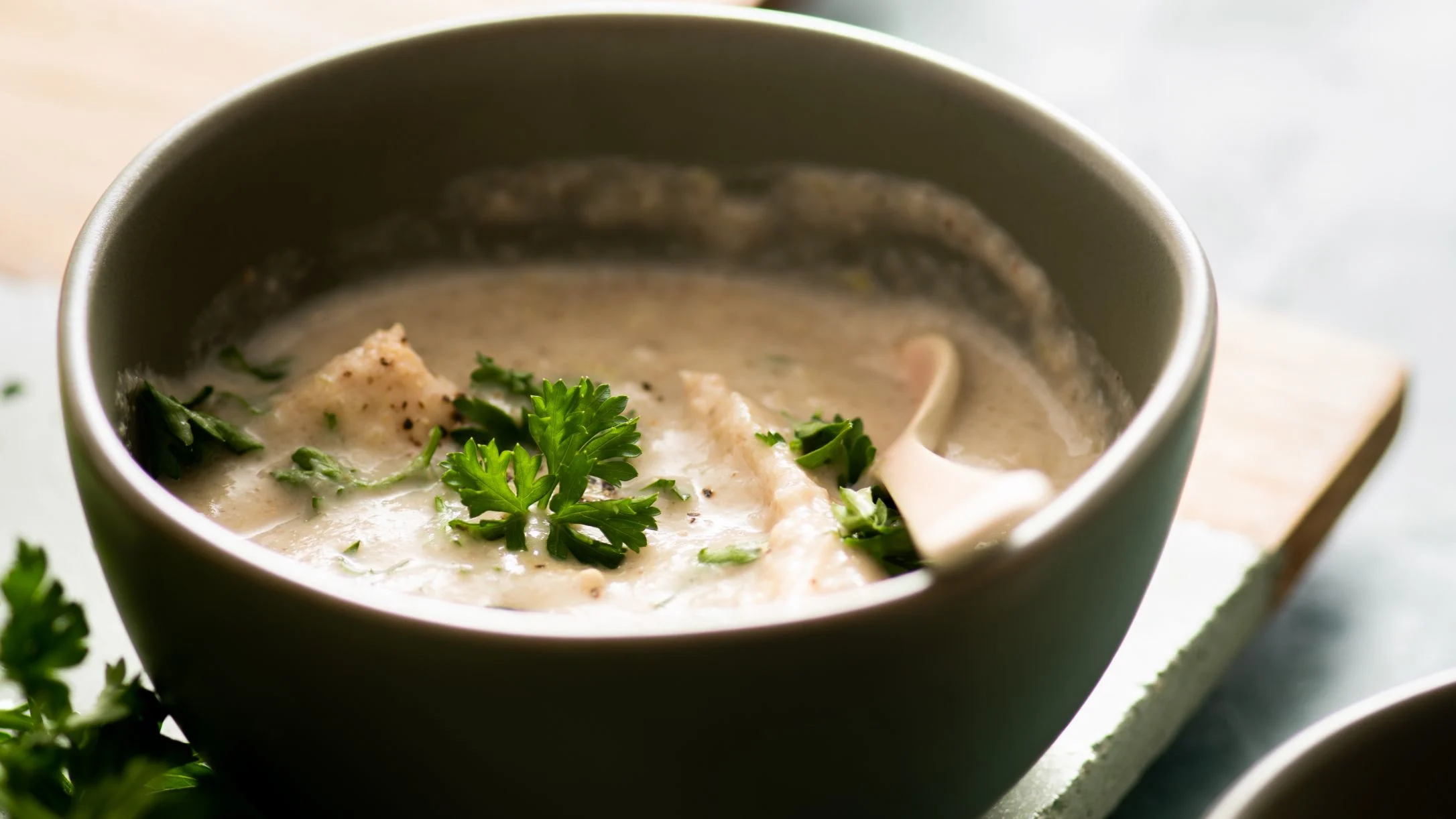 Creamy soup in a gray bowl garnished with fresh parsley, featuring chunks of chicken and mushroom.