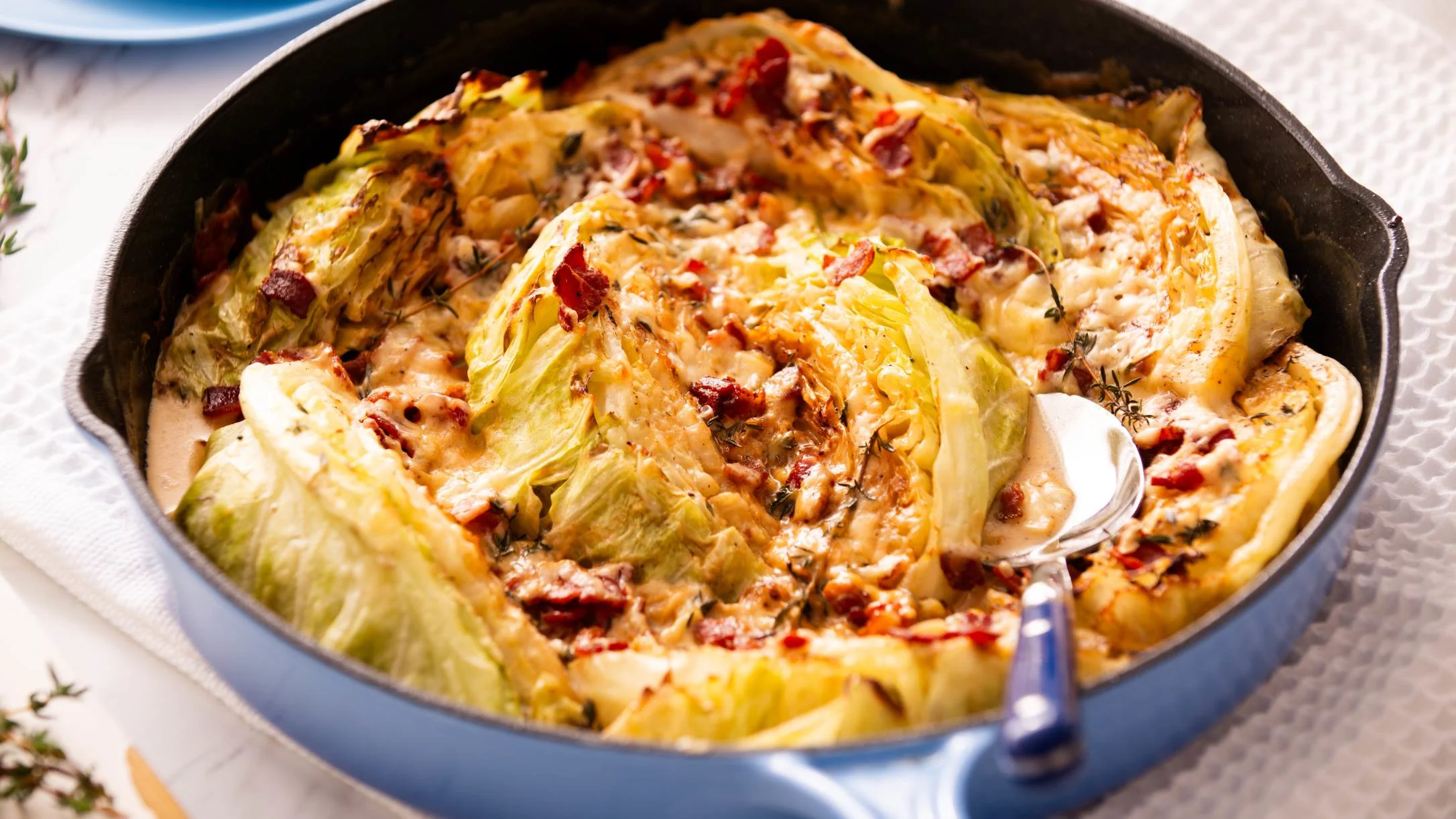 Roasted cabbage wedges in a cast iron skillet with creamy sauce and bacon bits, served with a silver spoon.
