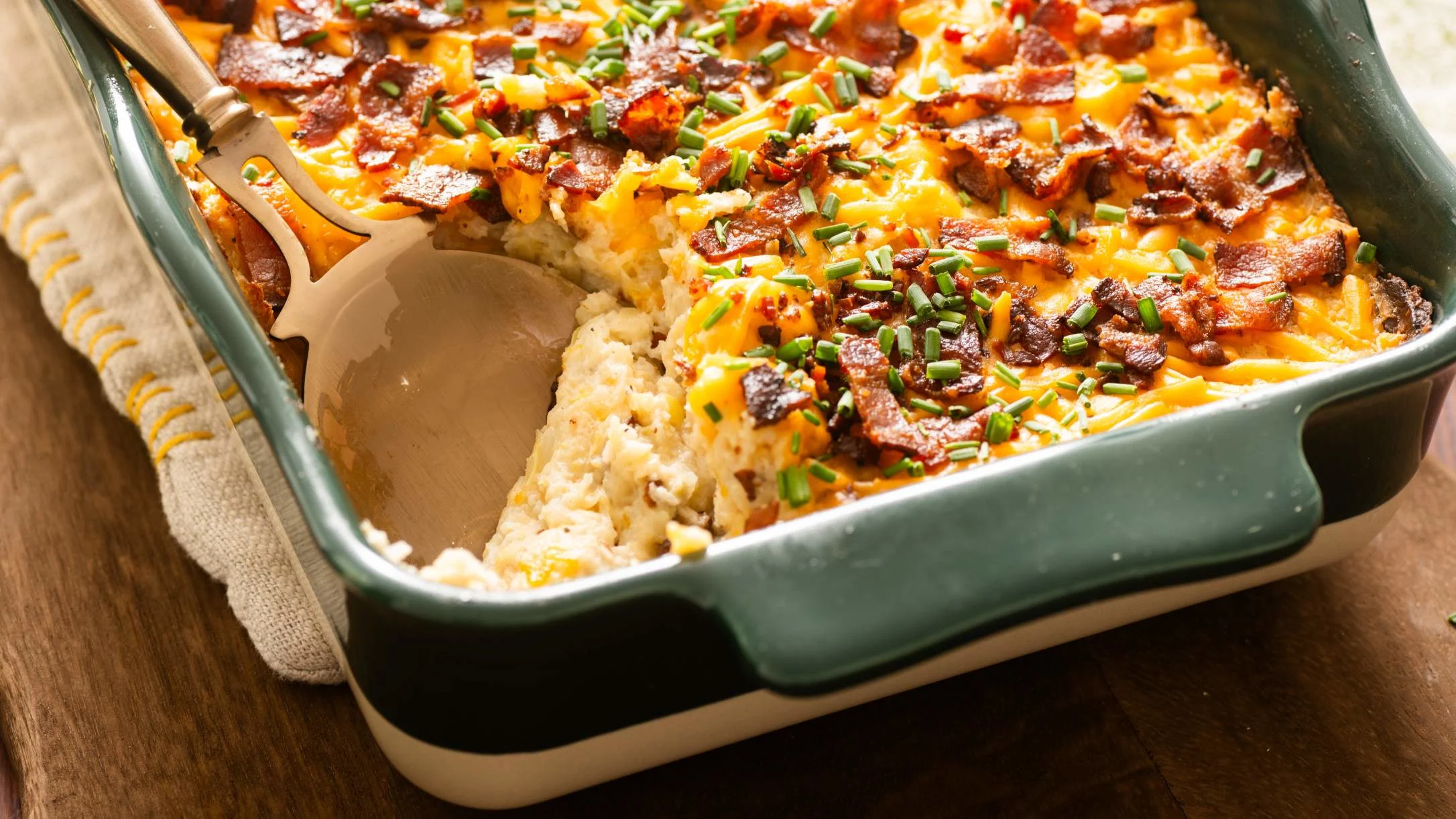 Creamy faux potato casserole topped with melted cheese, crispy bacon bits, and fresh green chives in a green baking dish.
