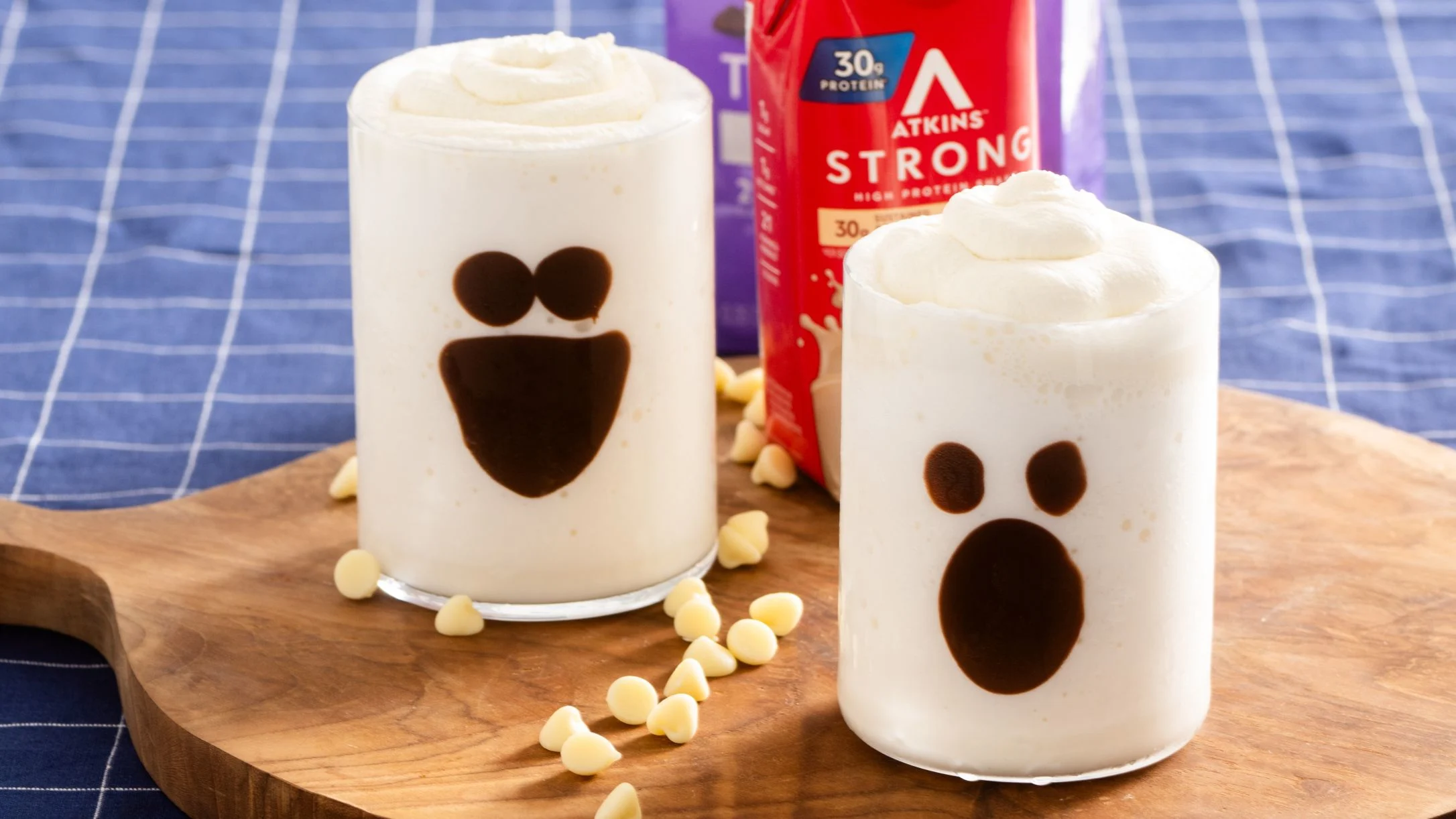 Two white cocktails with chocolate ghost faces on wooden board, Atkins protein drink in background.