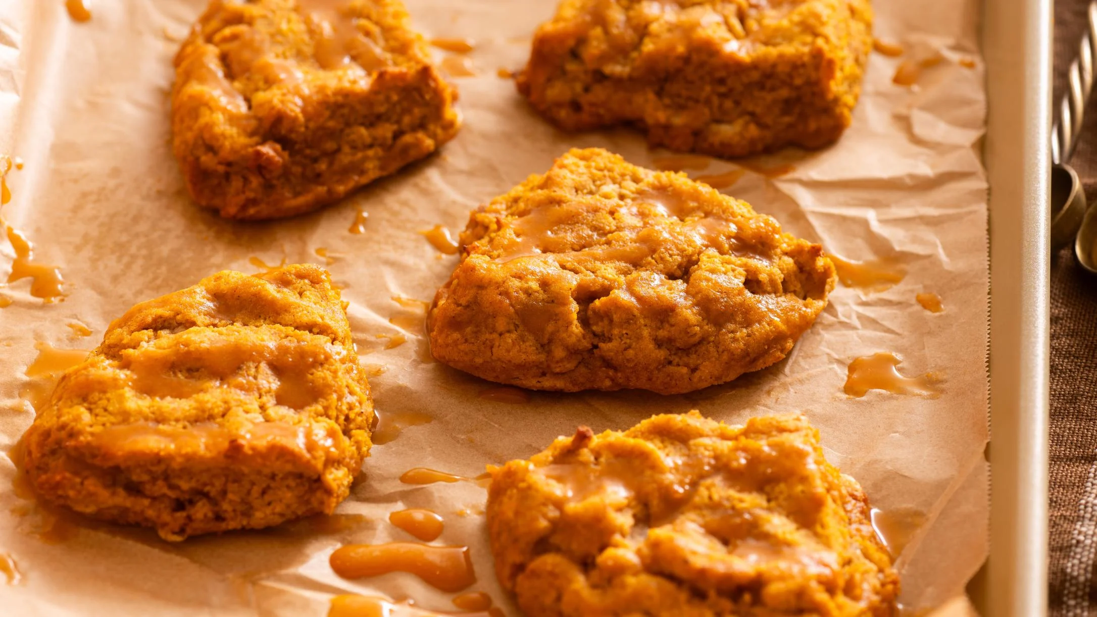 Freshly baked pumpkin cookies with pumpkin protein drizzle on parchment paper in a baking tray.