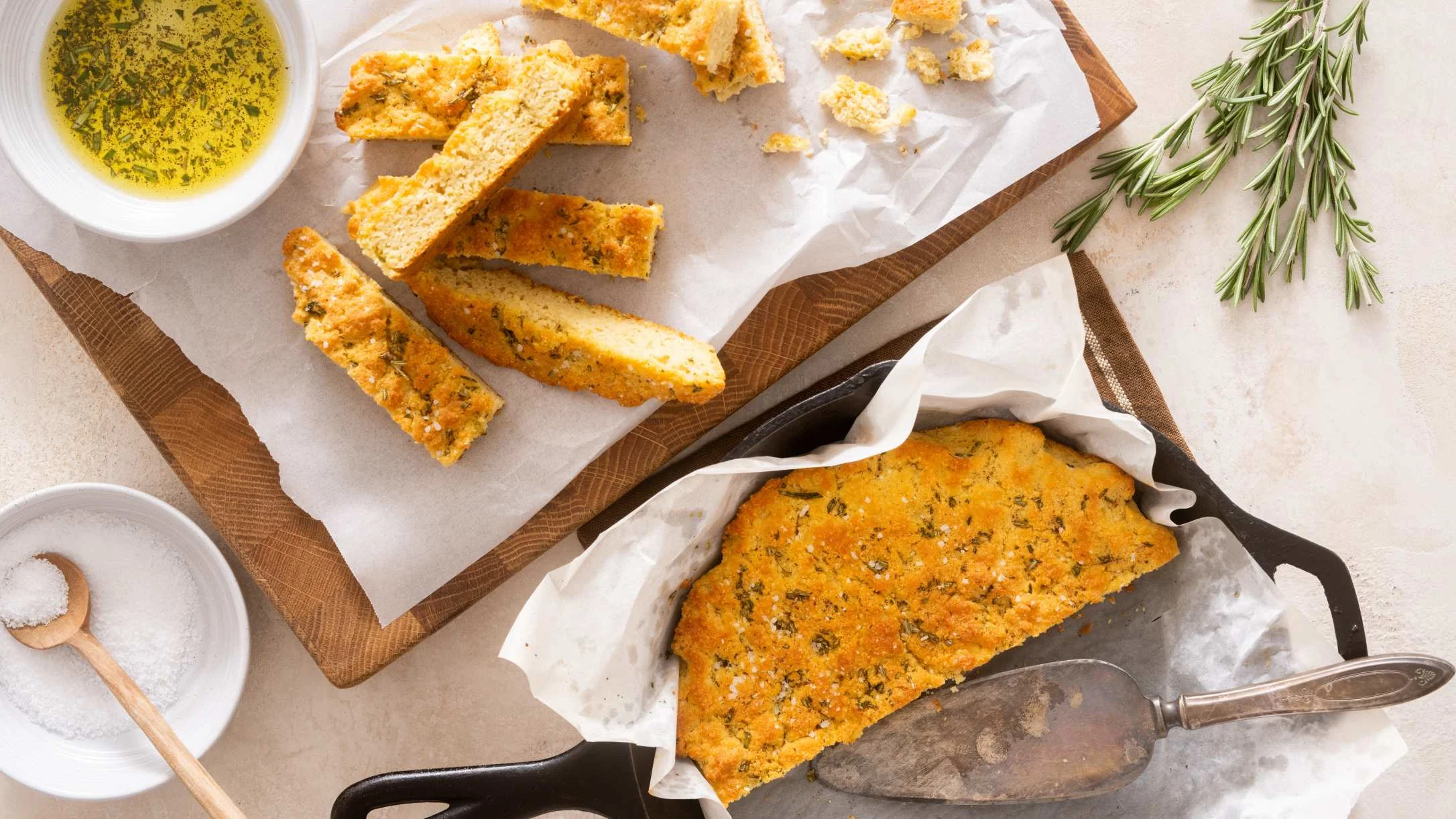 Homemade herb bread with sliced pieces on parchment paper, served with herb-infused oil and salt on the side.