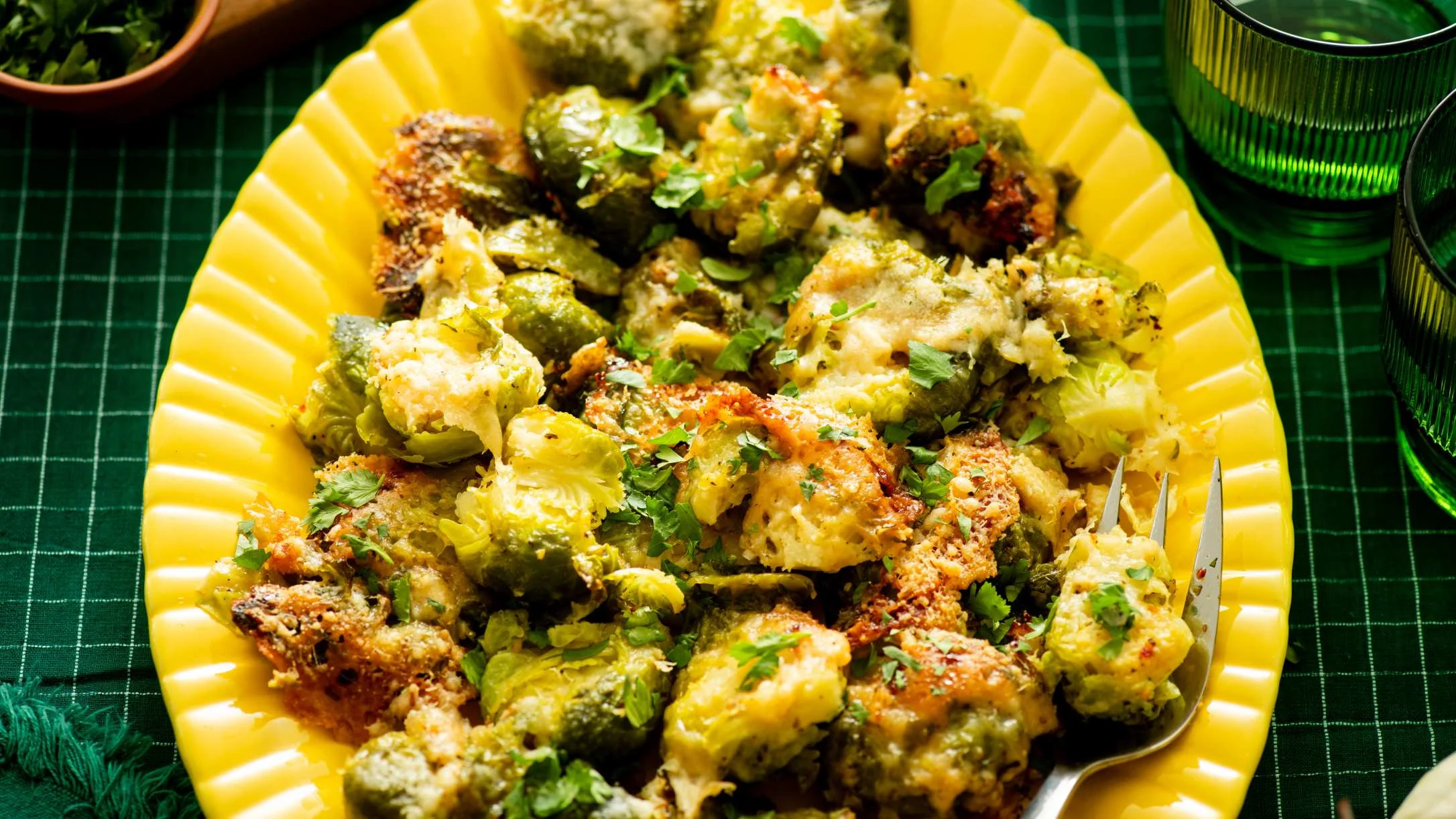 Roasted Brussels sprouts with cheese and herbs served in a bright yellow dish on a green tablecloth.