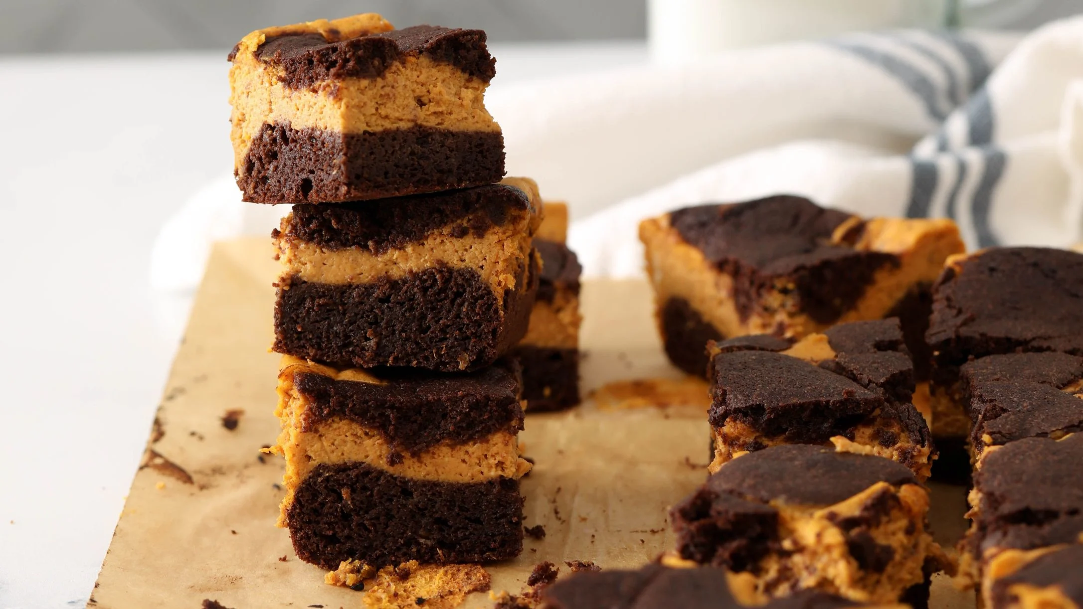 Stacked chocolate and pumpkin brownies on parchment paper with more brownies scattered nearby.