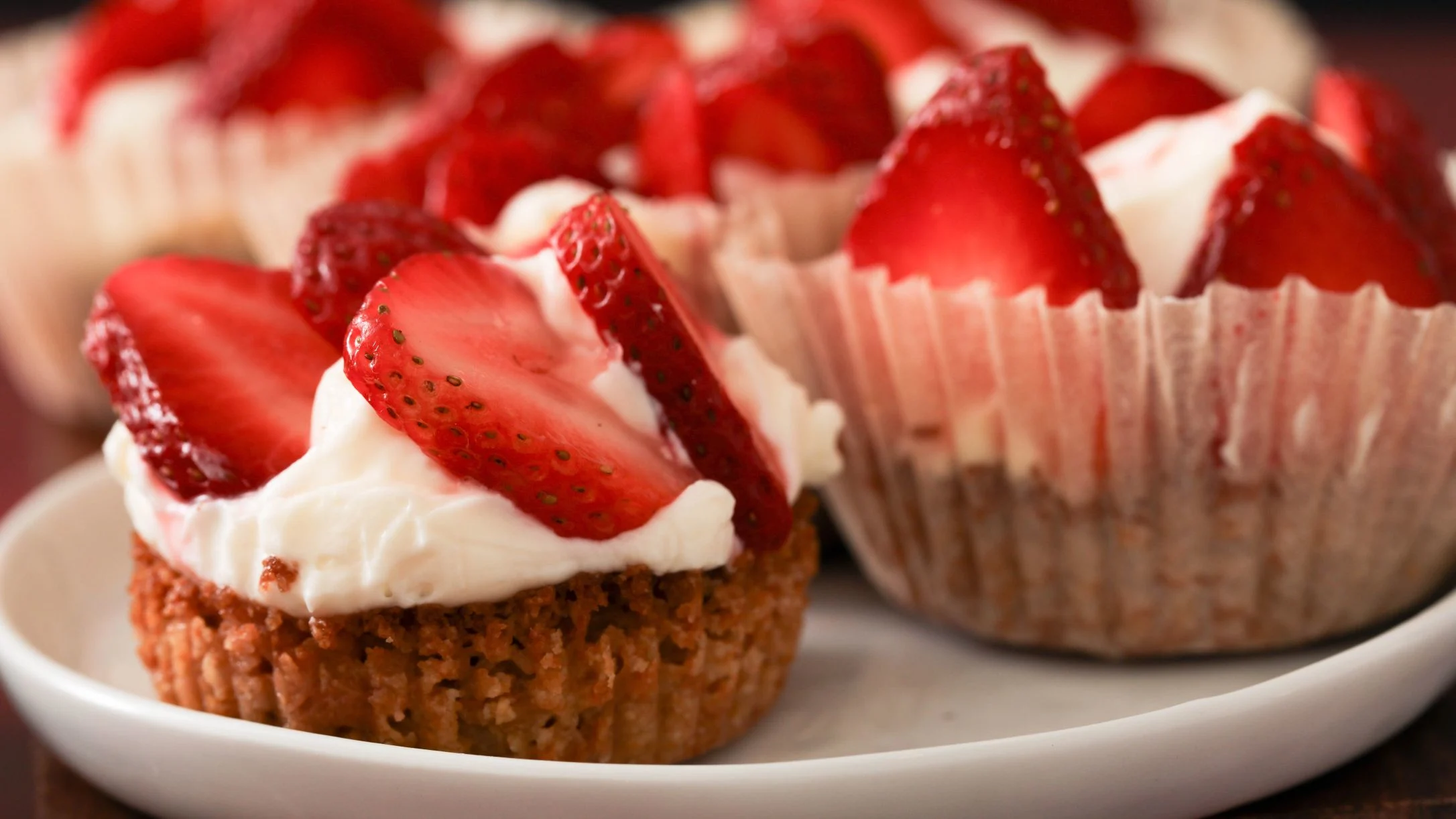 Mini strawberry tarts with cream filling and fresh sliced strawberries on top, served on a white plate.