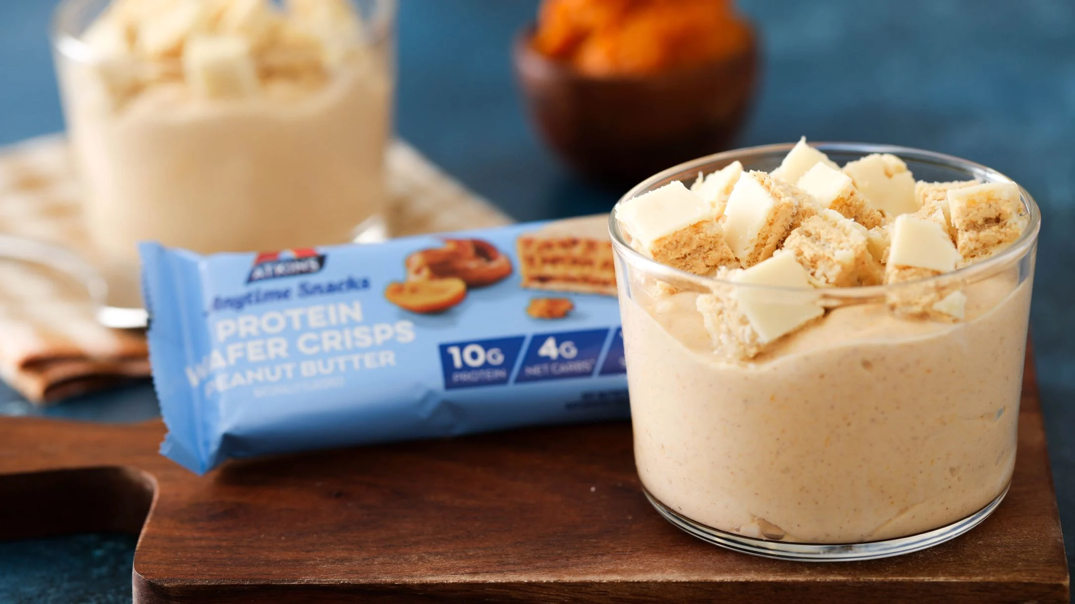 Creamy yogurt cups topped with protein wafer bar pieces alongside a peanut butter protein wafer bar on wooden board.