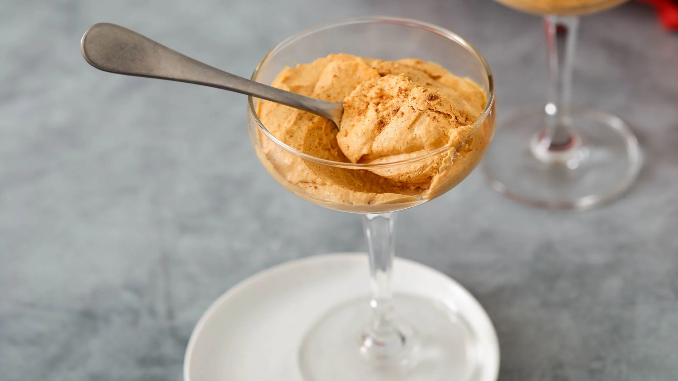 Creamy pumpkin mousse served in an elegant glass dessert cup with a metal spoon on marble surface.