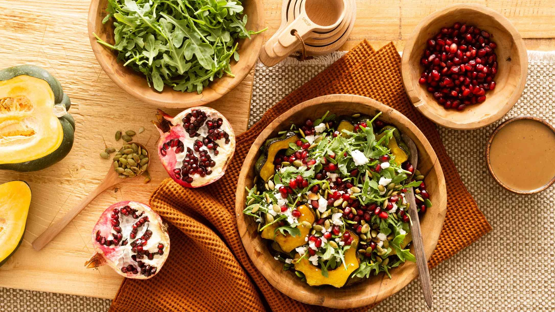 Wooden bowls with fresh salad featuring arugula, squash, pomegranate seeds, and pumpkin seeds on a rustic wooden table.