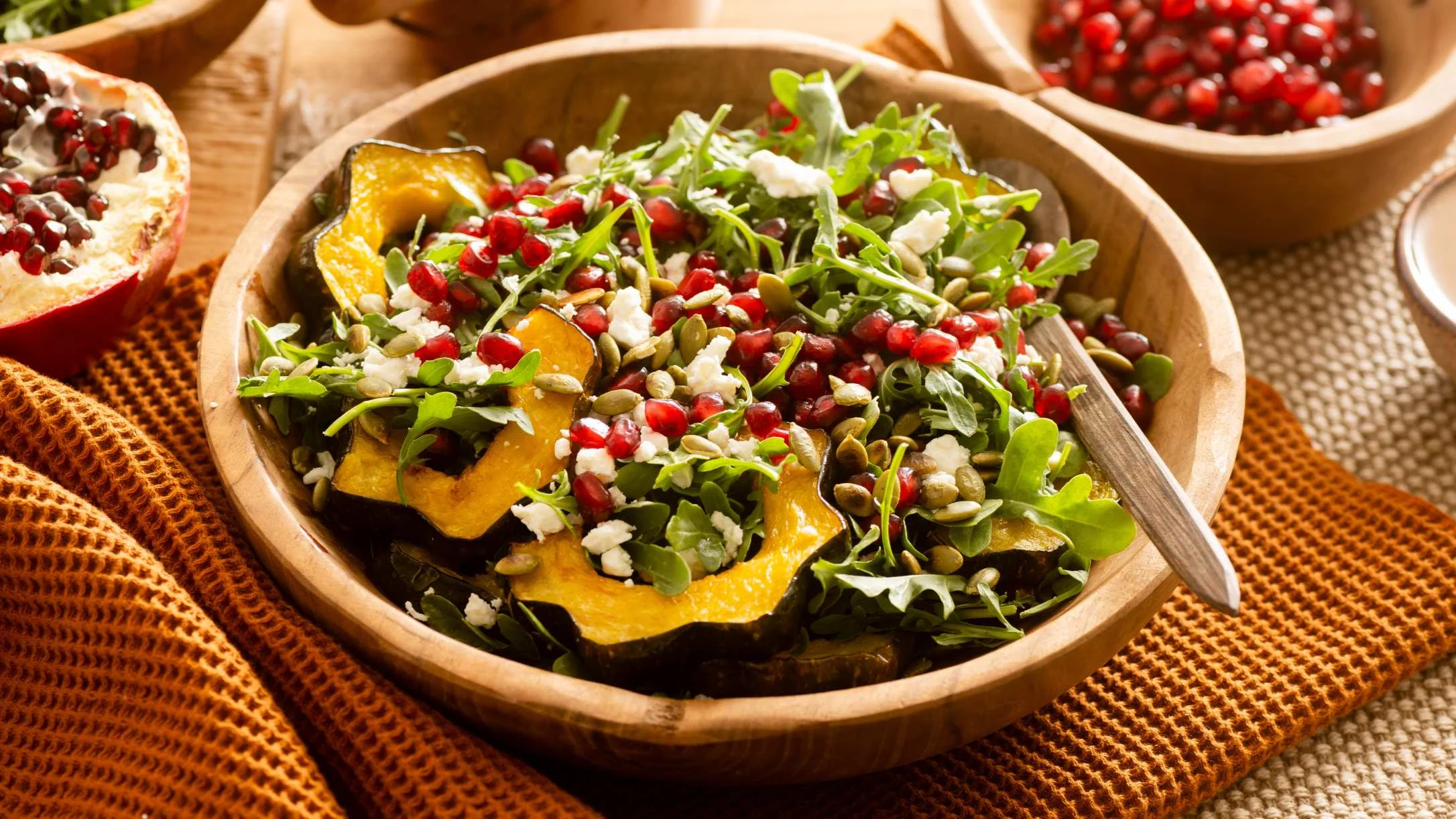 Wooden bowl of autumn salad with roasted squash, arugula, pomegranate seeds, feta cheese and pumpkin seeds.