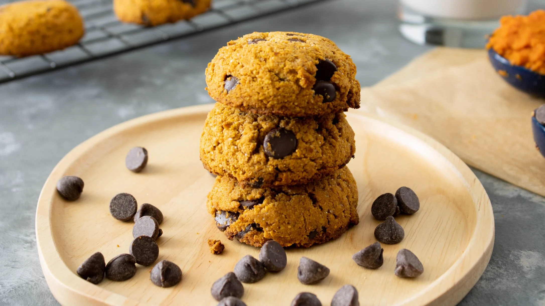 Stack of golden pumpkin chocolate chip cookies on a wooden plate with chocolate chips scattered around.