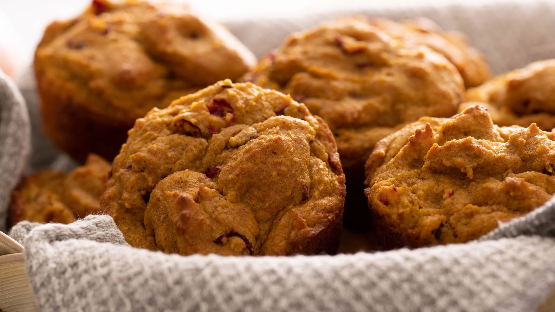 Freshly baked golden-brown muffins with berry bits nestled in a cloth-lined basket, shown in close-up.